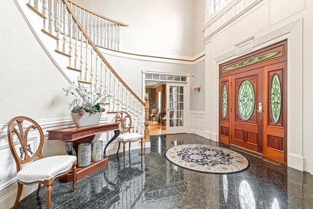 foyer entrance with plenty of natural light, a towering ceiling, a wainscoted wall, granite finish floor, and a decorative wall