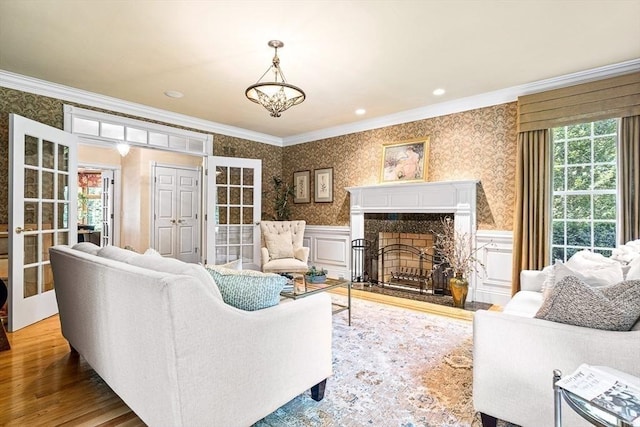 living area featuring crown molding, a healthy amount of sunlight, wainscoting, and wallpapered walls