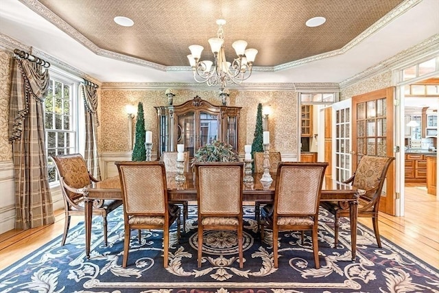 dining room with wainscoting, a raised ceiling, light wood-style flooring, and wallpapered walls