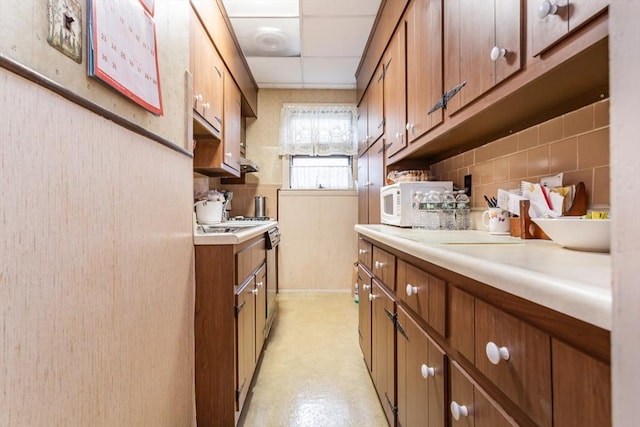 kitchen with white microwave, backsplash, light countertops, brown cabinetry, and a paneled ceiling