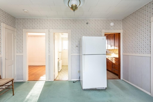 kitchen featuring wallpapered walls, carpet, radiator heating unit, wainscoting, and freestanding refrigerator