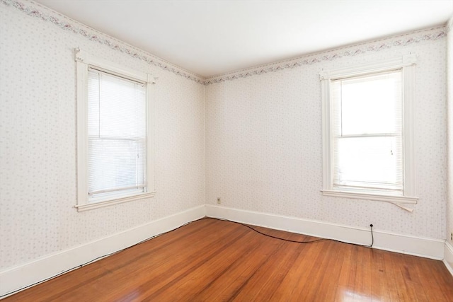 spare room with wallpapered walls, wood finished floors, and baseboards