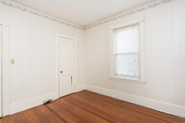 unfurnished room with wallpapered walls, wood finished floors, and baseboards