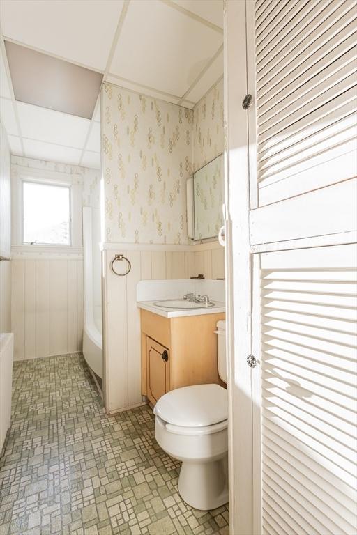 bathroom featuring toilet, wainscoting, wallpapered walls, a bathtub, and vanity