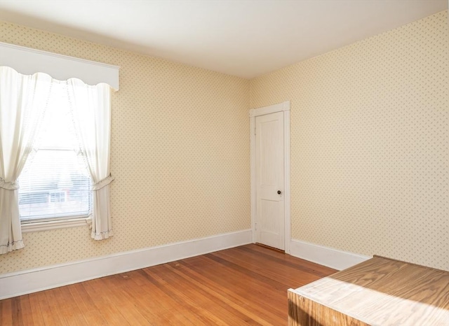 unfurnished bedroom with wallpapered walls, wood finished floors, and baseboards