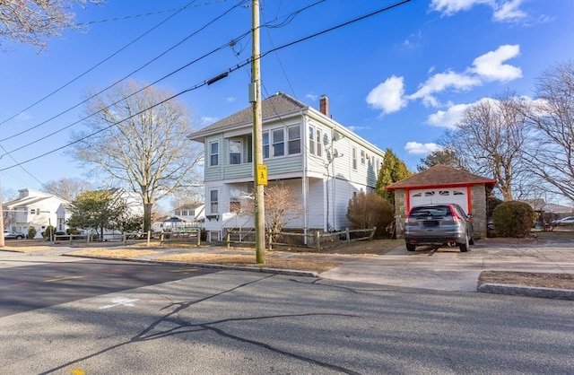 view of front of home with a detached garage, an outbuilding, concrete driveway, and a chimney