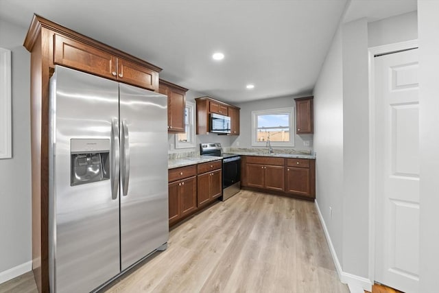 kitchen with sink, light hardwood / wood-style flooring, light stone countertops, and appliances with stainless steel finishes