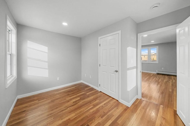 unfurnished room with baseboard heating and light hardwood / wood-style flooring