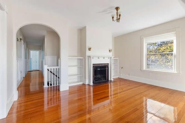 4-6 W St, Arlington, MA 02476 - unfurnished living room featuring arched walkways, wood finished floors, a fireplace with flush hearth, built in features, and baseboards