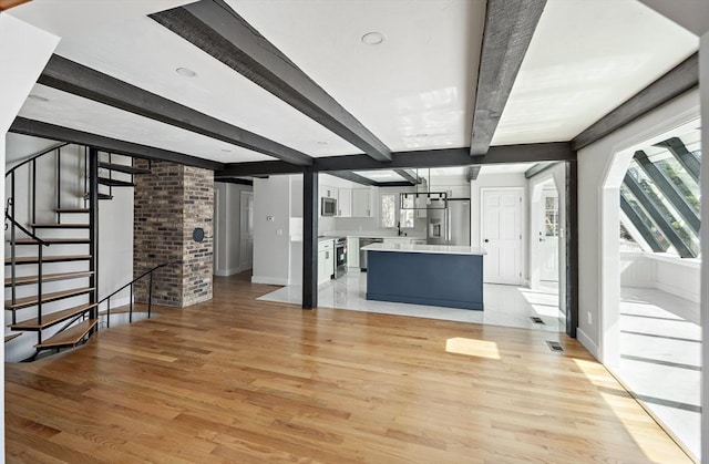 unfurnished living room featuring light wood-type flooring, beam ceiling, and a wealth of natural light