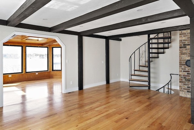 unfurnished living room with arched walkways, baseboards, beamed ceiling, wood finished floors, and stairs