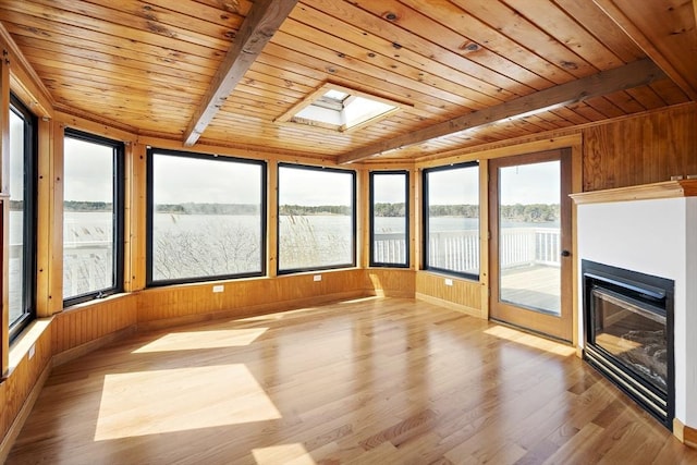 unfurnished sunroom featuring wooden walls, wood finished floors, a water view, a skylight, and wood ceiling