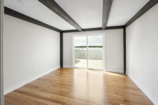 unfurnished room featuring baseboards, beam ceiling, and light wood finished floors