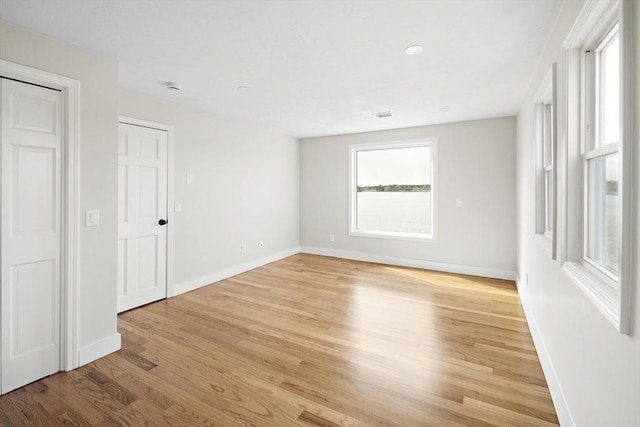 unfurnished room with light wood-type flooring, visible vents, and baseboards