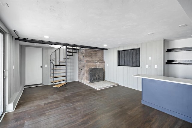 unfurnished living room featuring recessed lighting, wood finished floors, a brick fireplace, and stairs