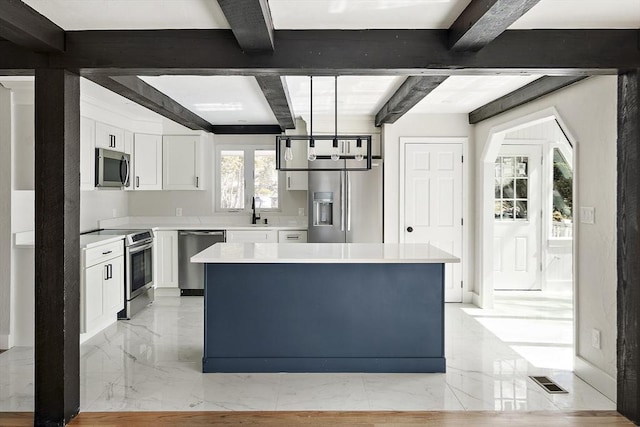 kitchen featuring a center island, stainless steel appliances, beamed ceiling, light countertops, and white cabinets