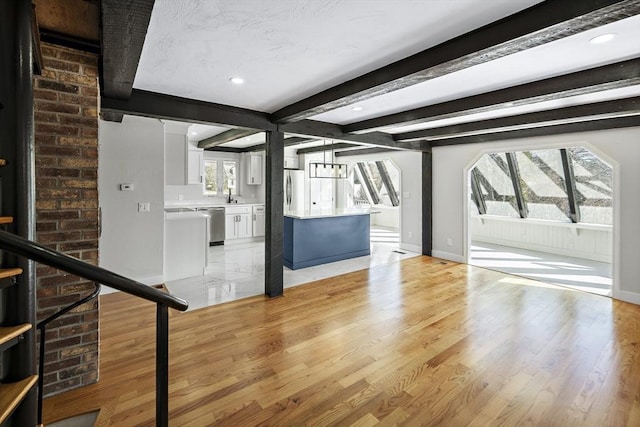 unfurnished living room with plenty of natural light, stairs, beamed ceiling, and light wood-type flooring