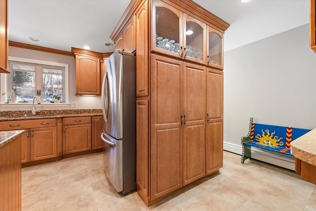 kitchen featuring brown cabinets, glass insert cabinets, freestanding refrigerator, a sink, and light stone countertops