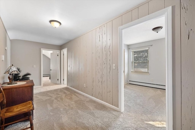 corridor with light carpet, wood walls, a baseboard radiator, and baseboards