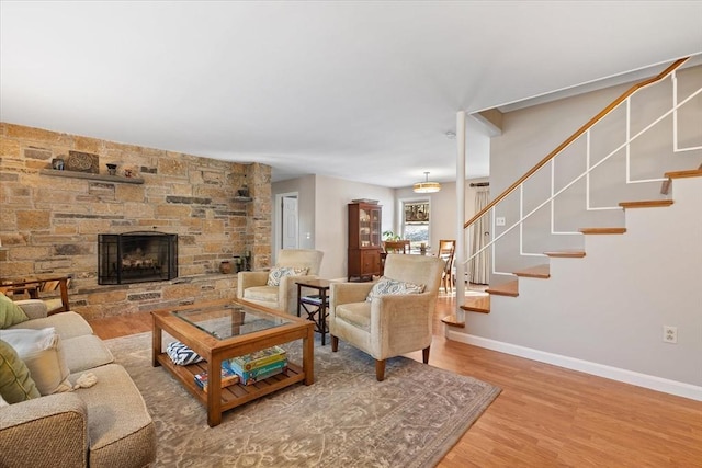 living area featuring a stone fireplace, stairway, wood finished floors, and baseboards