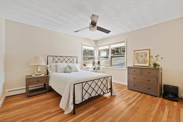 bedroom featuring ceiling fan, light wood finished floors, a baseboard radiator, and baseboards