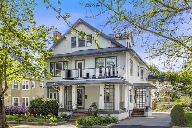 view of front of property with a balcony, a chimney, covered porch, and stucco siding