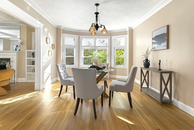 dining area featuring baseboards, light wood finished floors, a chandelier, ornamental molding, and a fireplace