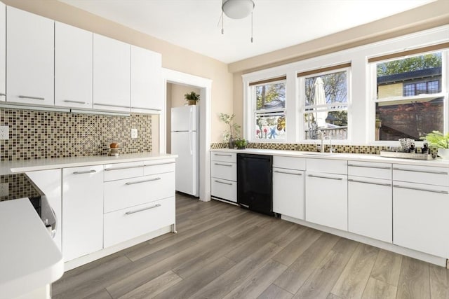 kitchen with black dishwasher, freestanding refrigerator, decorative backsplash, light countertops, and light wood finished floors