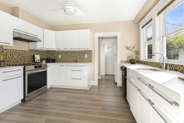 kitchen featuring under cabinet range hood, electric range, a sink, a ceiling fan, and decorative backsplash