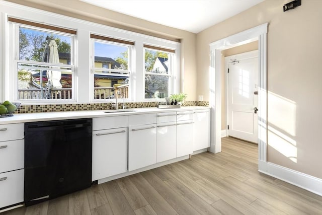 kitchen with black dishwasher, light countertops, light wood-style floors, white cabinets, and tasteful backsplash