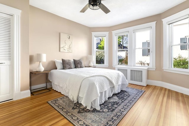 bedroom featuring radiator heating unit, multiple windows, baseboards, and light wood finished floors