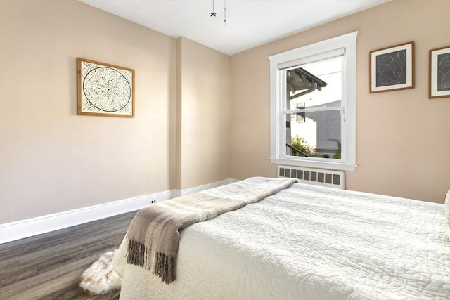 bedroom with radiator, wood finished floors, and baseboards
