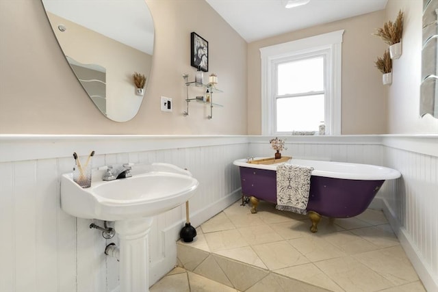 bathroom with a freestanding bath, wainscoting, a decorative wall, and tile patterned flooring