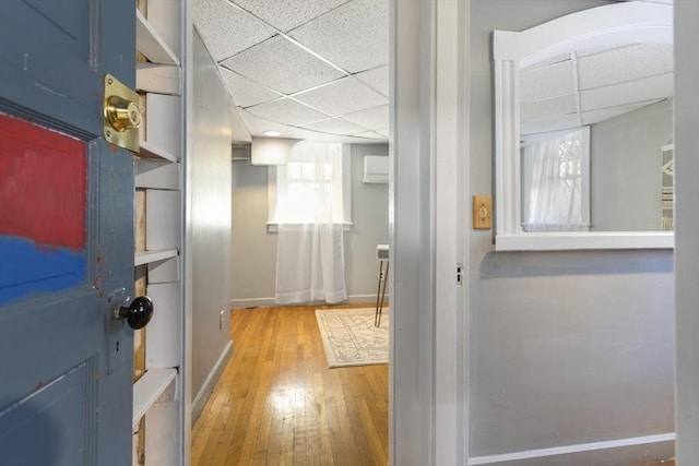 hall with baseboards, a drop ceiling, hardwood / wood-style floors, healthy amount of natural light, and an AC wall unit