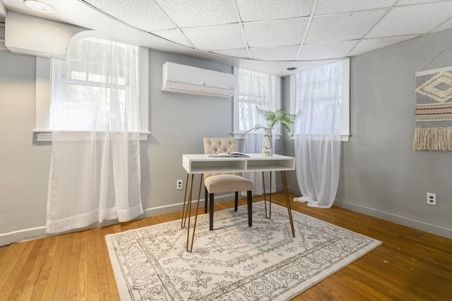 home office with a wall unit AC, wood finished floors, baseboards, and a drop ceiling