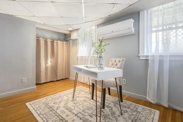 office space featuring a wall mounted air conditioner, a drop ceiling, baseboards, and wood finished floors