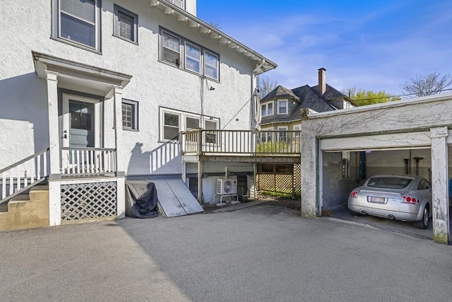 back of house with stucco siding, a garage, and a wooden deck