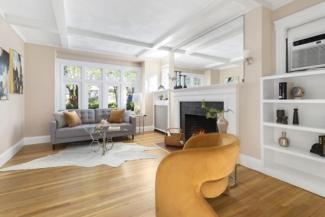 living area with coffered ceiling, baseboards, wood finished floors, a lit fireplace, and beam ceiling