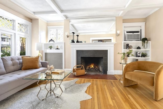 living area featuring coffered ceiling, a brick fireplace, wood finished floors, beam ceiling, and baseboards