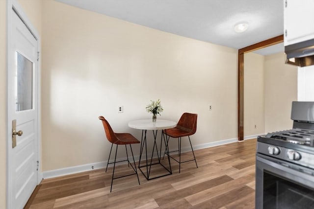 kitchen with white cabinets, gas stove, light hardwood / wood-style floors, and a breakfast bar