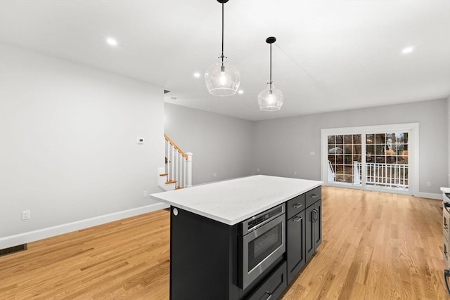 27 Leonard St Unit 27, Bridgewater, MA 02324 - kitchen with stainless steel microwave, dark cabinetry, a kitchen island, light wood finished floors, and recessed lighting