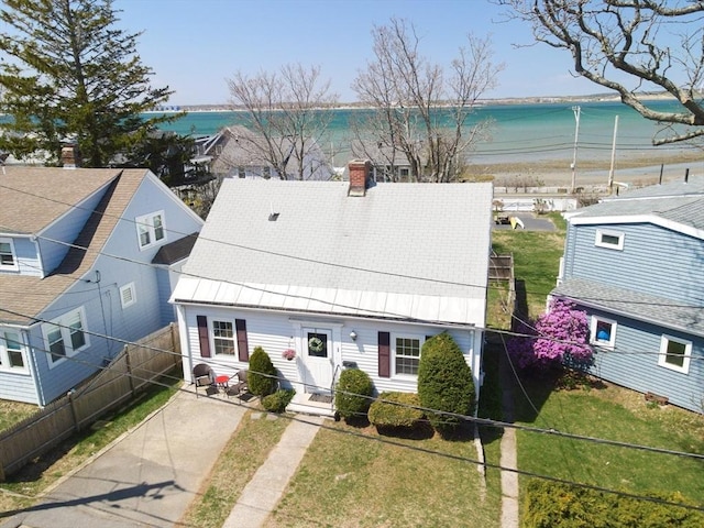 view of front of property featuring fence, a front yard, a chimney, a view of the beach, and a water view