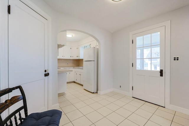 doorway to outside with light tile patterned floors, arched walkways, and baseboards