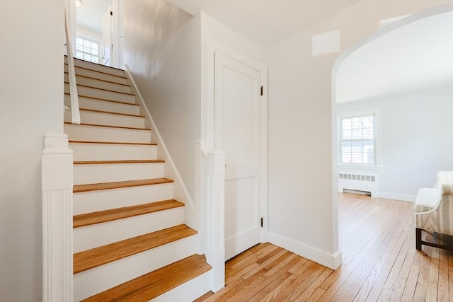 staircase featuring arched walkways, a wealth of natural light, hardwood / wood-style flooring, and radiator