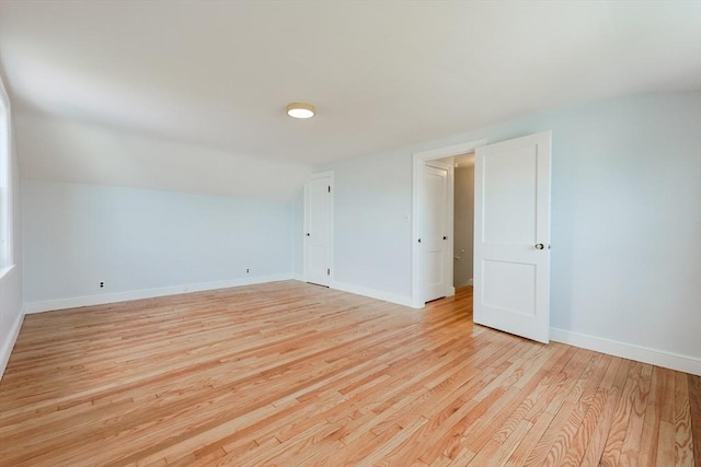 unfurnished room with baseboards, vaulted ceiling, and light wood-style flooring
