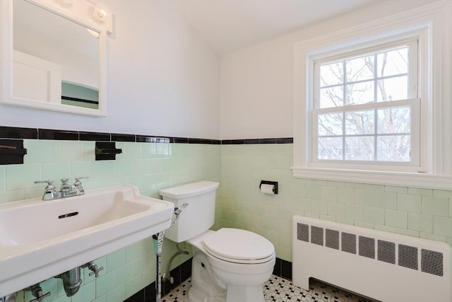bathroom featuring wainscoting, toilet, tile walls, radiator heating unit, and a sink