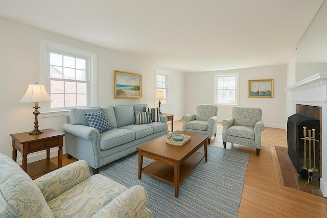 living room featuring baseboards, a brick fireplace, and light wood finished floors
