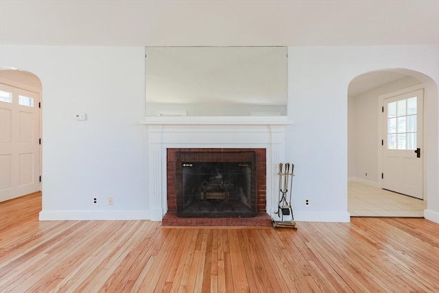 unfurnished living room with arched walkways, baseboards, a fireplace, and hardwood / wood-style floors