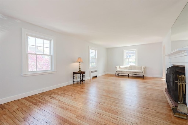 sitting room with radiator heating unit, baseboards, a fireplace with raised hearth, and light wood finished floors