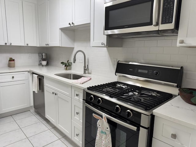 kitchen with light tile patterned floors, tasteful backsplash, white cabinets, stainless steel appliances, and a sink